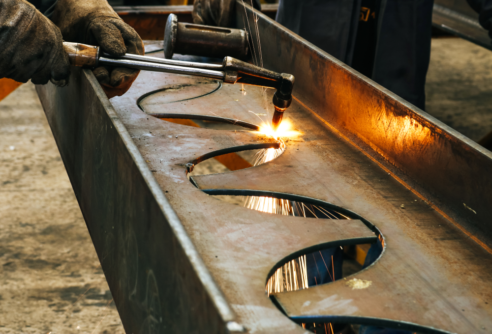 A welder uses a torch on curvy metal sheets, sparks flying, in a workshop setting. Protective gloves are worn